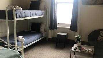 A dormitory room with bunk beds, a small table with a plant, and a window with curtains.
