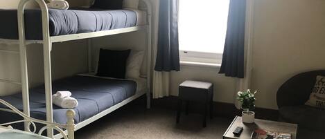 Un dormitorio con literas, una mesita con una planta y una ventana con cortinas.