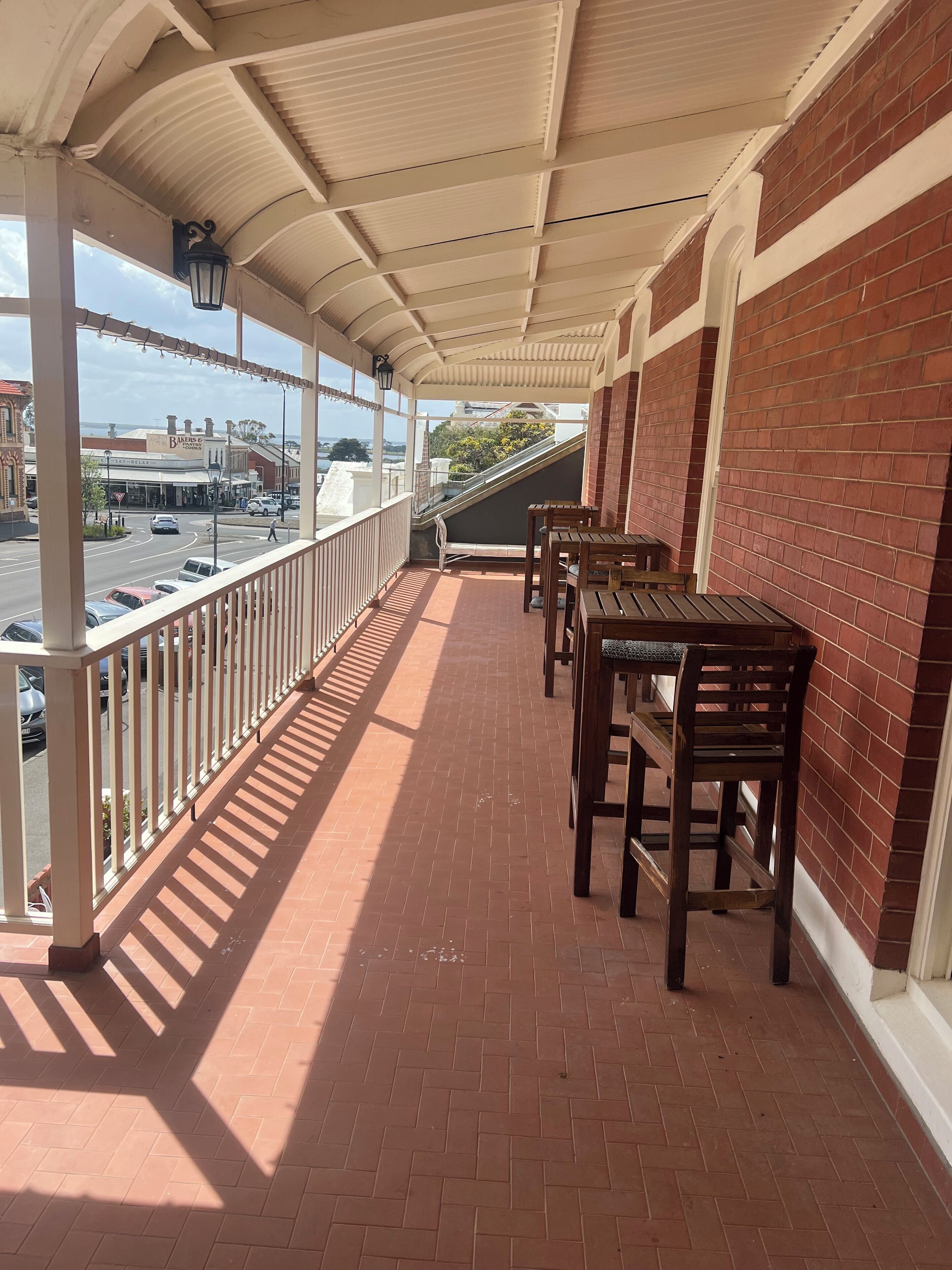 A covered balcony with brick flooring and wooden tables and chairs.