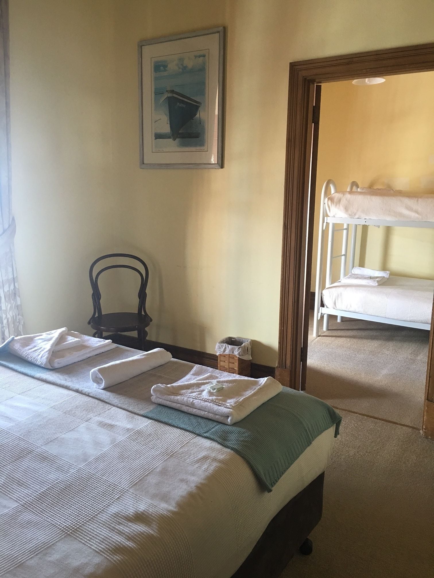 A hotel room with a bed, a chair, a small table, and a painting on the wall.