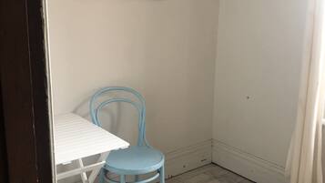 A room with a white table and two blue chairs, a woven rug, and a painting on the wall.