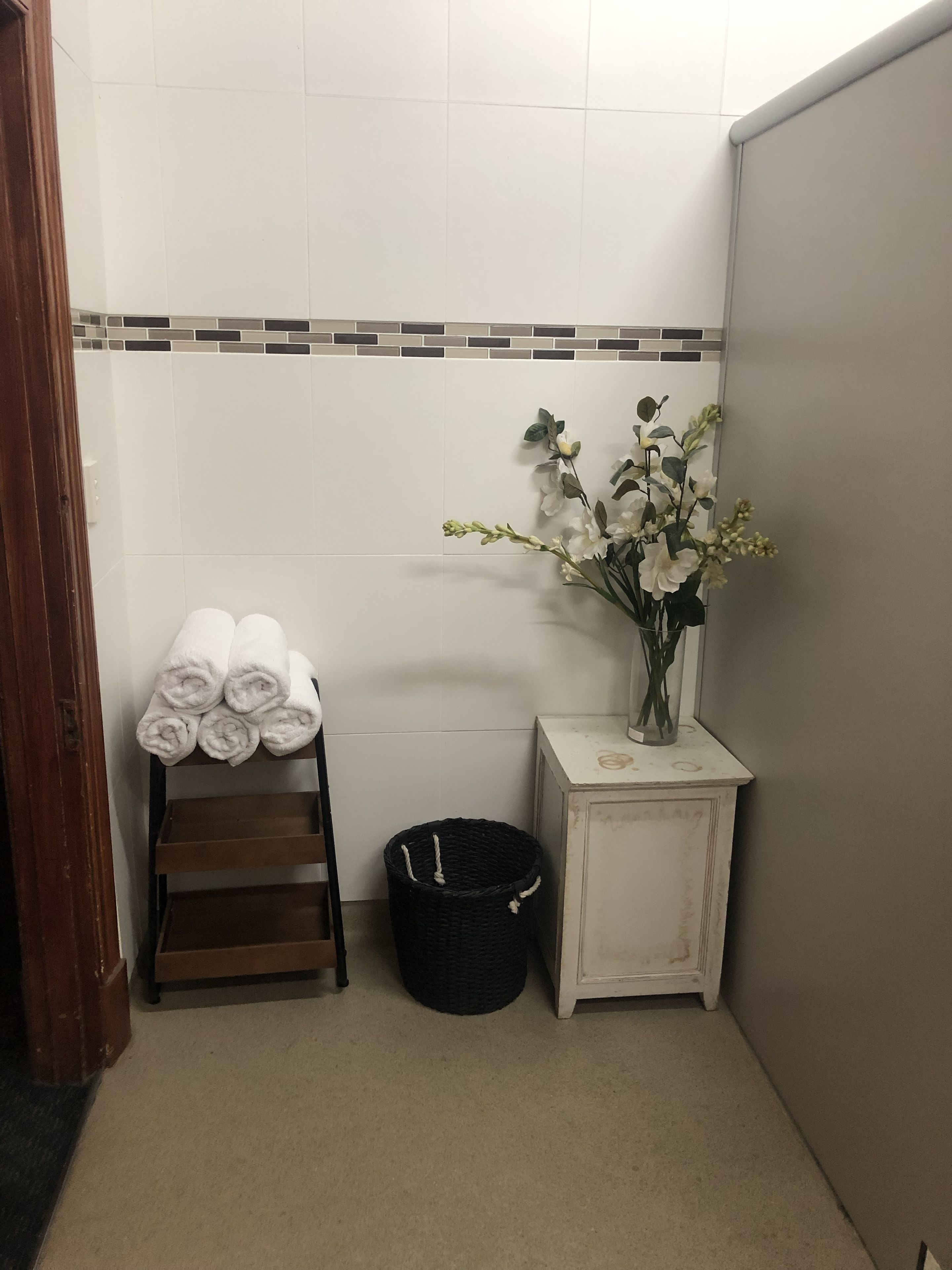 A bathroom with a towel rack, a trash bin, and a vase with flowers.