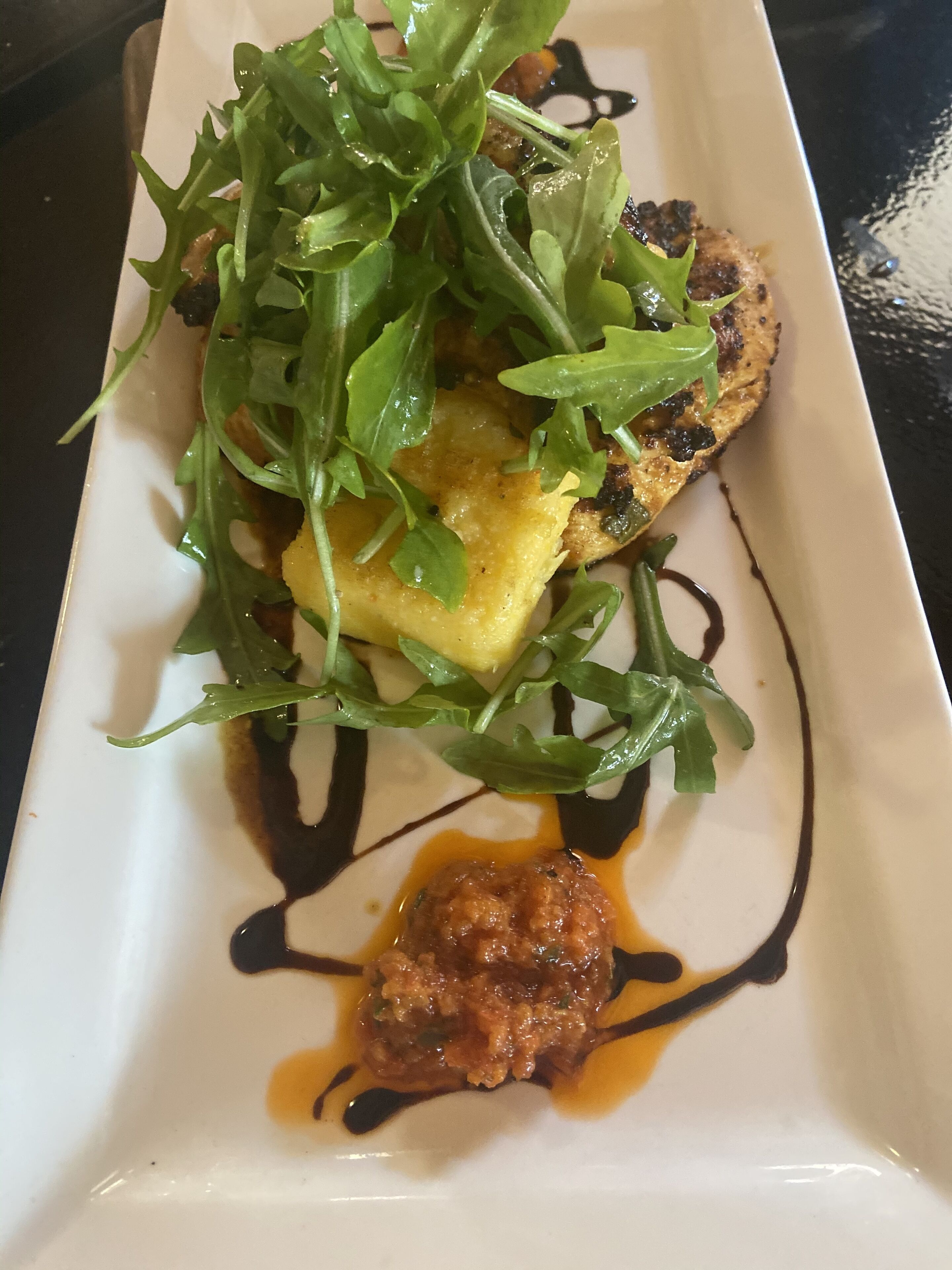 Un plat rectangular blanc amb una galeta a la planxa, rúcula i una cullerada de salsa.