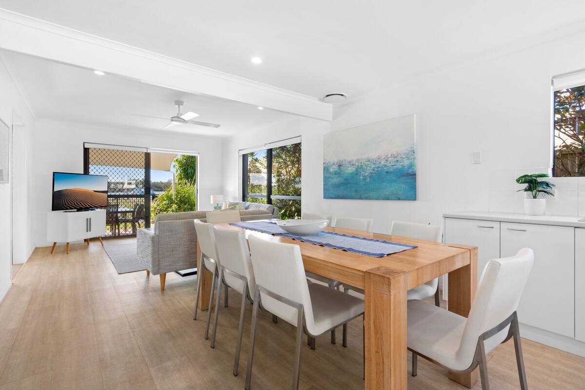 A modern dining area with a wooden table, white chairs, and a large painting on the wall.