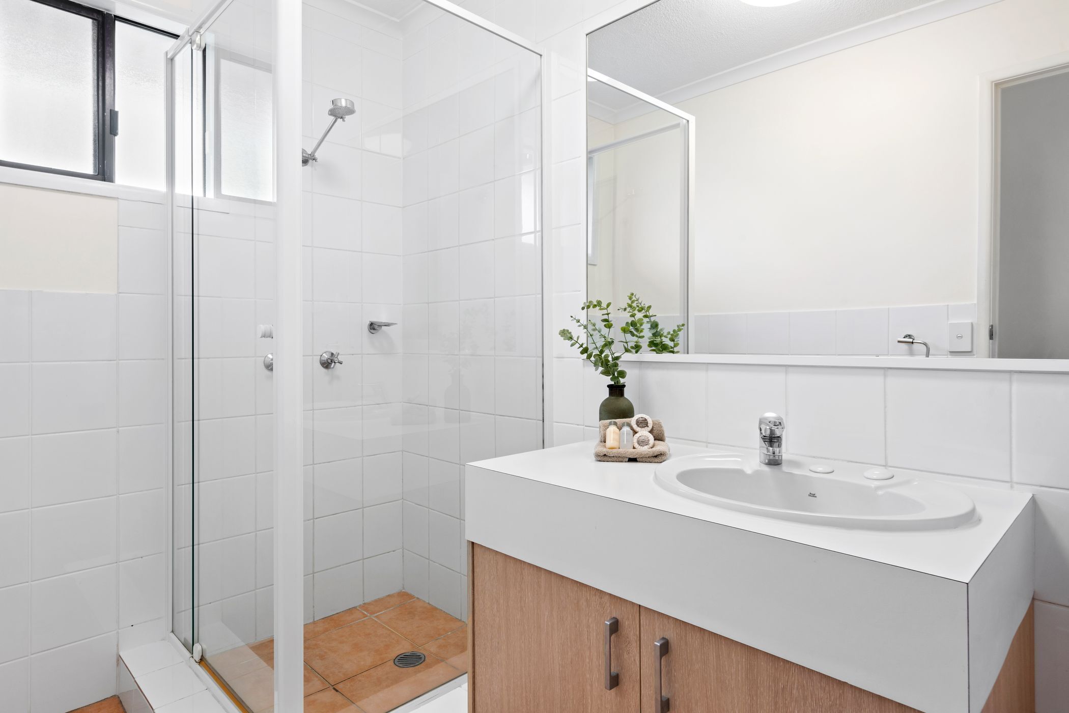 A modern bathroom with a glass shower enclosure, a white sink, and a mirror above it.