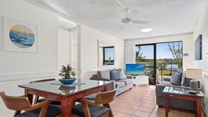 A modern living room with a dining table, chairs, a sofa, and a TV. - Cayman Quays (Noosaville)