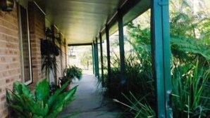 A covered outdoor corridor with brick walls, potted plants, and a view of greenery outside. - Bulahdelah Myall Motel (Bulahdelah)