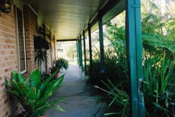 A covered outdoor corridor with brick walls, potted plants, and a view of greenery outside.