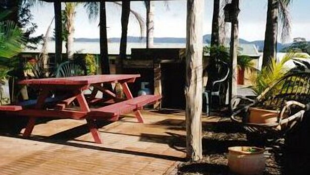 A wooden picnic table under a wooden pergola with a view of the sea. - Bulahdelah Myall Motel (Bulahdelah)