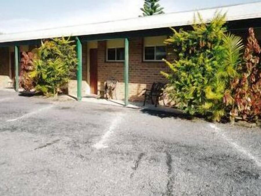 Un motel con estacionamiento techado, un edificio de ladrillo y diversas plantas.