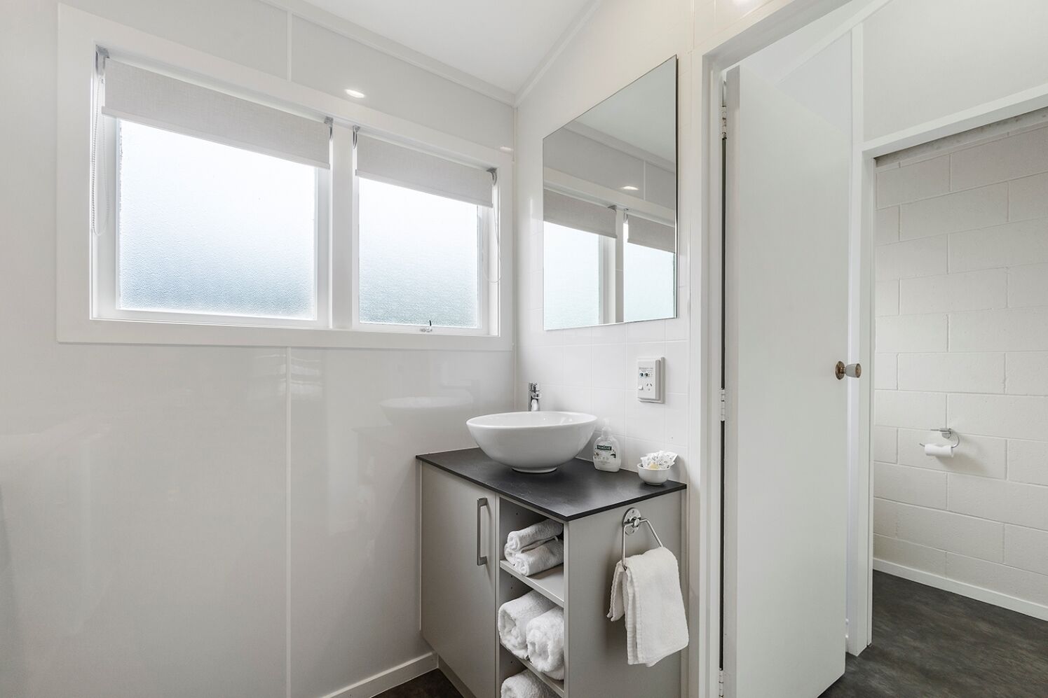 Een moderne badkamer met een witte wastafel, een grote spiegel en een raam met geëtste glas.
