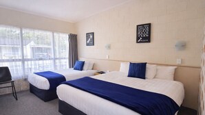 A hotel room with two beds, a chair, and a window with curtains. - Tower Road Motel (Matamata)