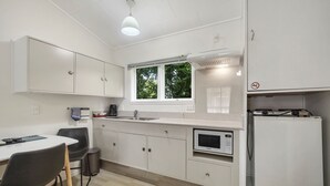 A modern kitchen with white cabinets, a built-in microwave, and a window with a view of greenery. - Tower Road Motel (Matamata)