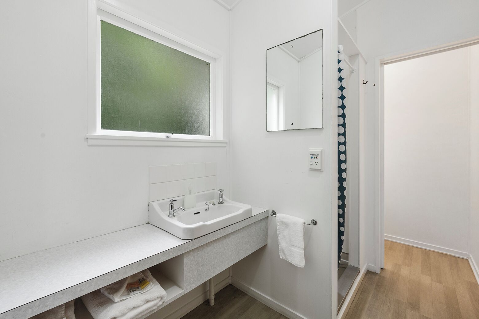 A modern bathroom with a white sink, a mirror, and a window.