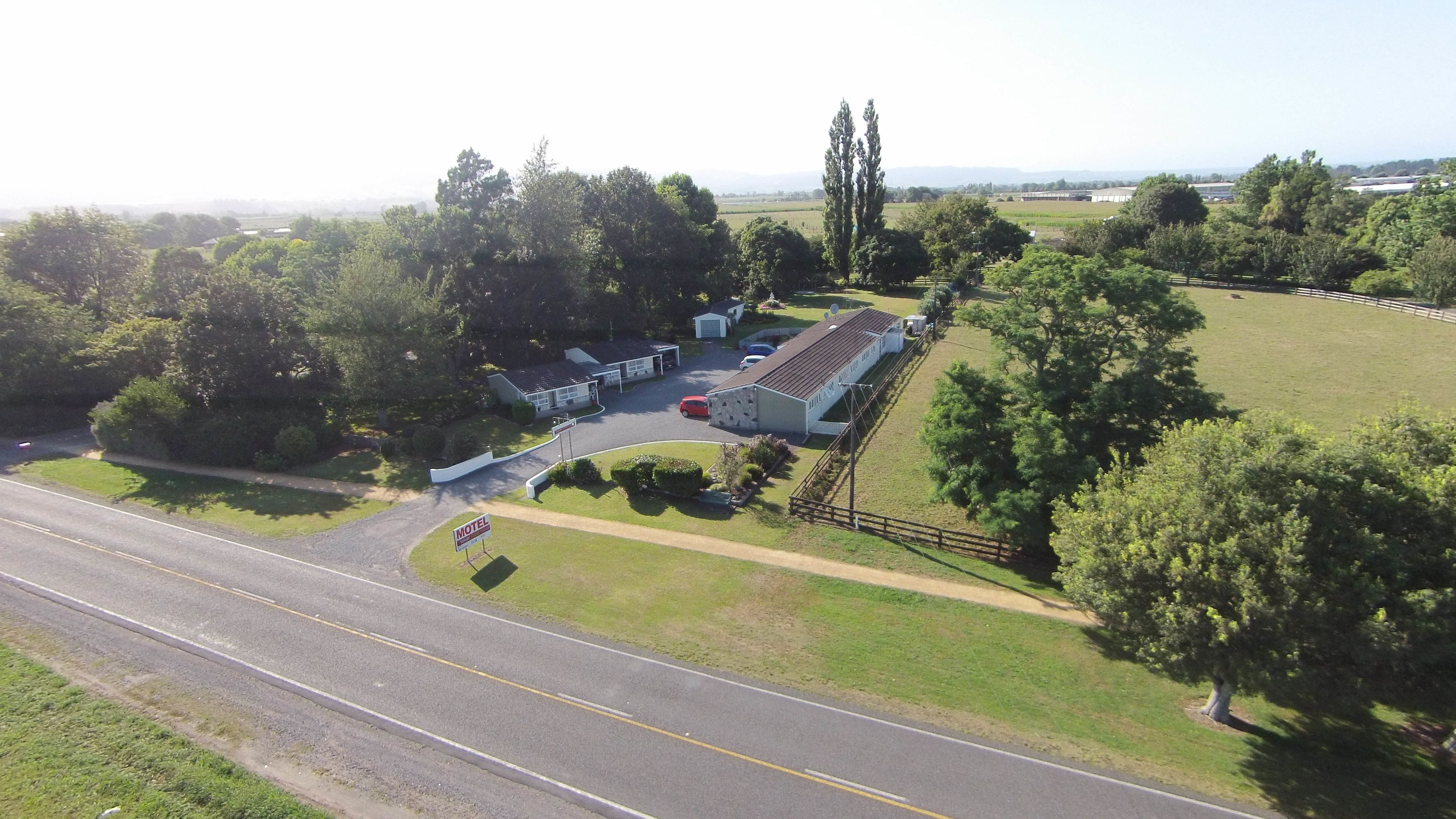 An aerial view of a motel with a large building, a parking area, and surrounding greenery.