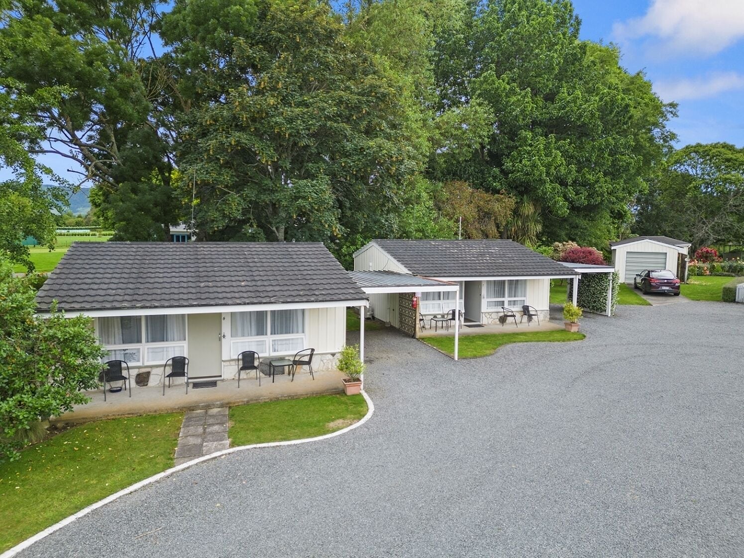 A row of small, single-story cabins with attached patios, surrounded by lush greenery and a clear sky.