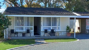 A small, single-story building with a tiled roof and a porch with four chairs. - Tower Road Motel (Matamata)