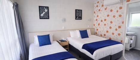 Ein Hotelzimmer mit zwei Betten, einem Nachttisch, einem kleinen Tisch und einem Badezimmer mit Waschbecken und Spiegel.