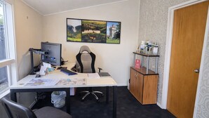 A small office with a desk, computer, and chair. There is a bookshelf with books and a small cabinet with a sign. - Tower Road Motel (Matamata)