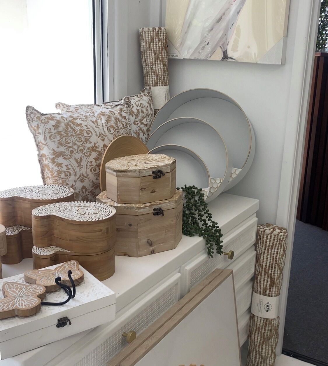 Una presentación de cajas de madera, platos decorativos y almohadones estampados sobre un tocador blanco.