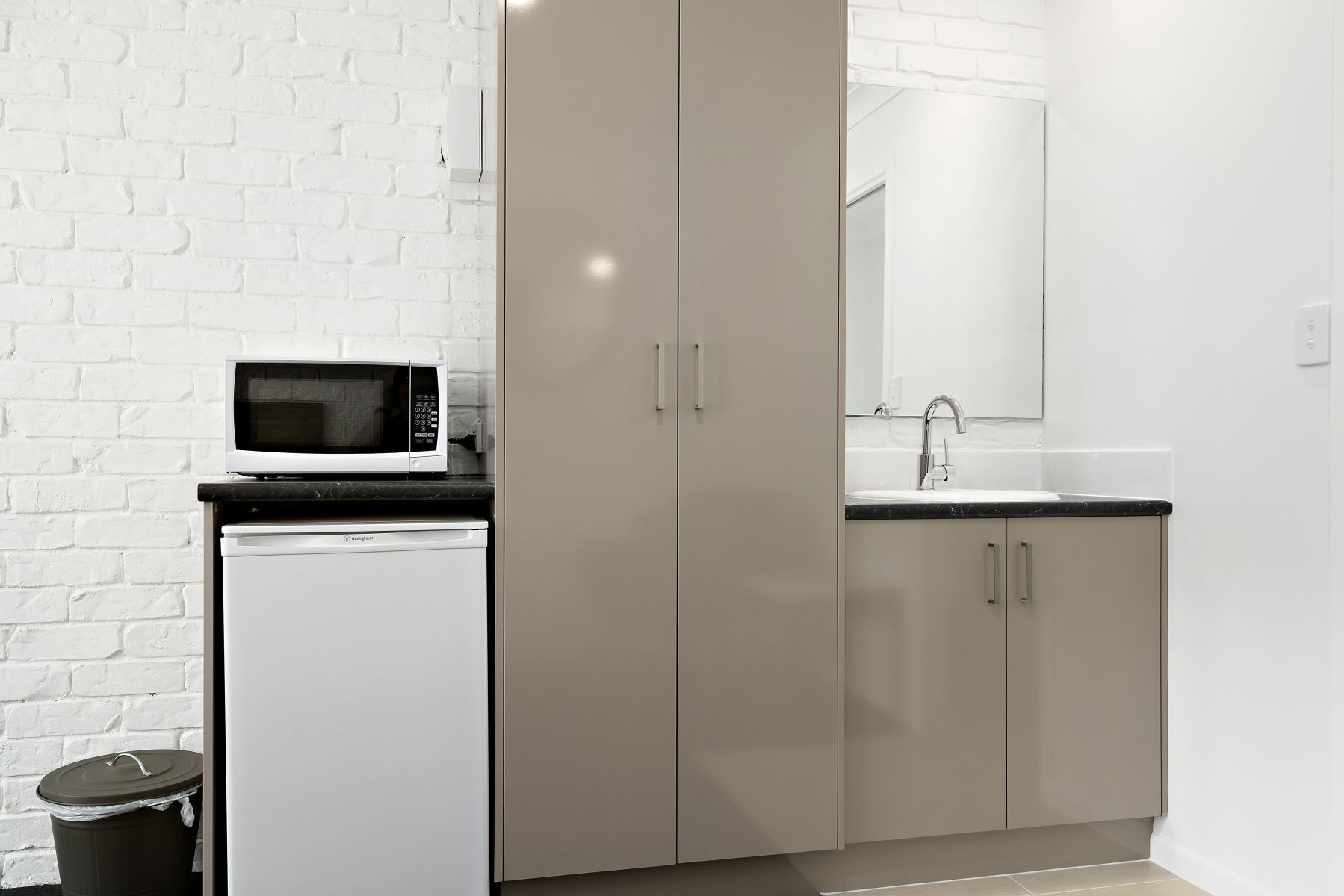 Una cocina compacta con microondas, un lavamanos y armarios.