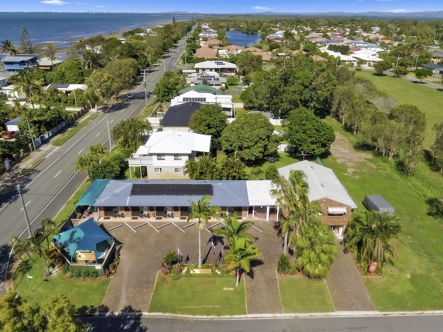 An aerial view of a coastal residential area with a prominent hotel featuring a large parking lot and a covered outdoor seating area.