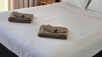 A hotel room with a bed, two towels, a nightstand, a wall-mounted air conditioner, and a window with curtains.