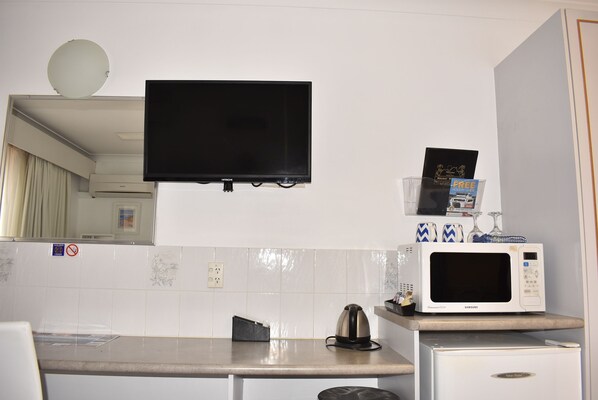A compact kitchen with a microwave, kettle, and a flat-screen TV mounted above the counter. - Port O'call Motel (Port Macquarie)