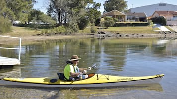 A man in a yellow kayak labeled "BARRACUDA" on a calm lake with a dock in the background and houses nearby.