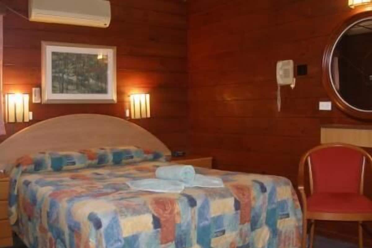 A wooden room with a bed, a chair, and wall-mounted lights.