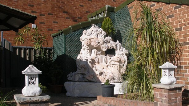 A courtyard with a stone sculpture, a small garden, and a brick wall. - Mount Kuring-Gai Motel (Mount Kuring-gai)