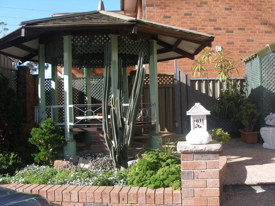 Un jardín con plantas y flores rodea un pabellón con techo de celosía.