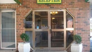 A reception area with a glass door, a brick facade, and two potted plants. - Mount Kuring-Gai Motel (Mount Kuring-gai)