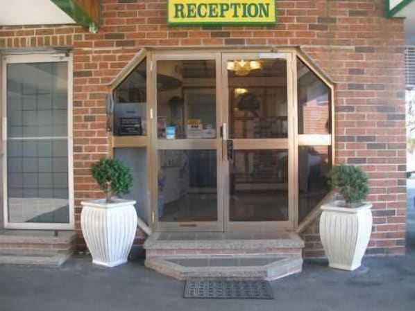 Un área de recepción con puerta de vidrio, fachada de ladrillo y dos plantas en macetas.