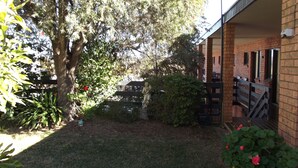 Un patio con un árbol grande, una estatua y un edificio de ladrillo con mesas al aire libre.