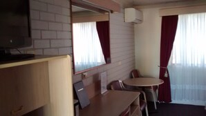 Habitación compacta con televisión sobre un mueble de madera, una mesita con sillas, un espejo y una ventana con cortinas.
