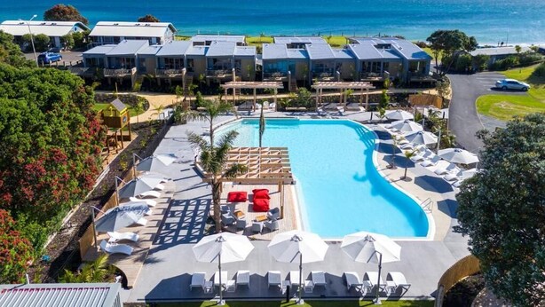 A resort with a large swimming pool surrounded by sun loungers and umbrellas, with ocean views.