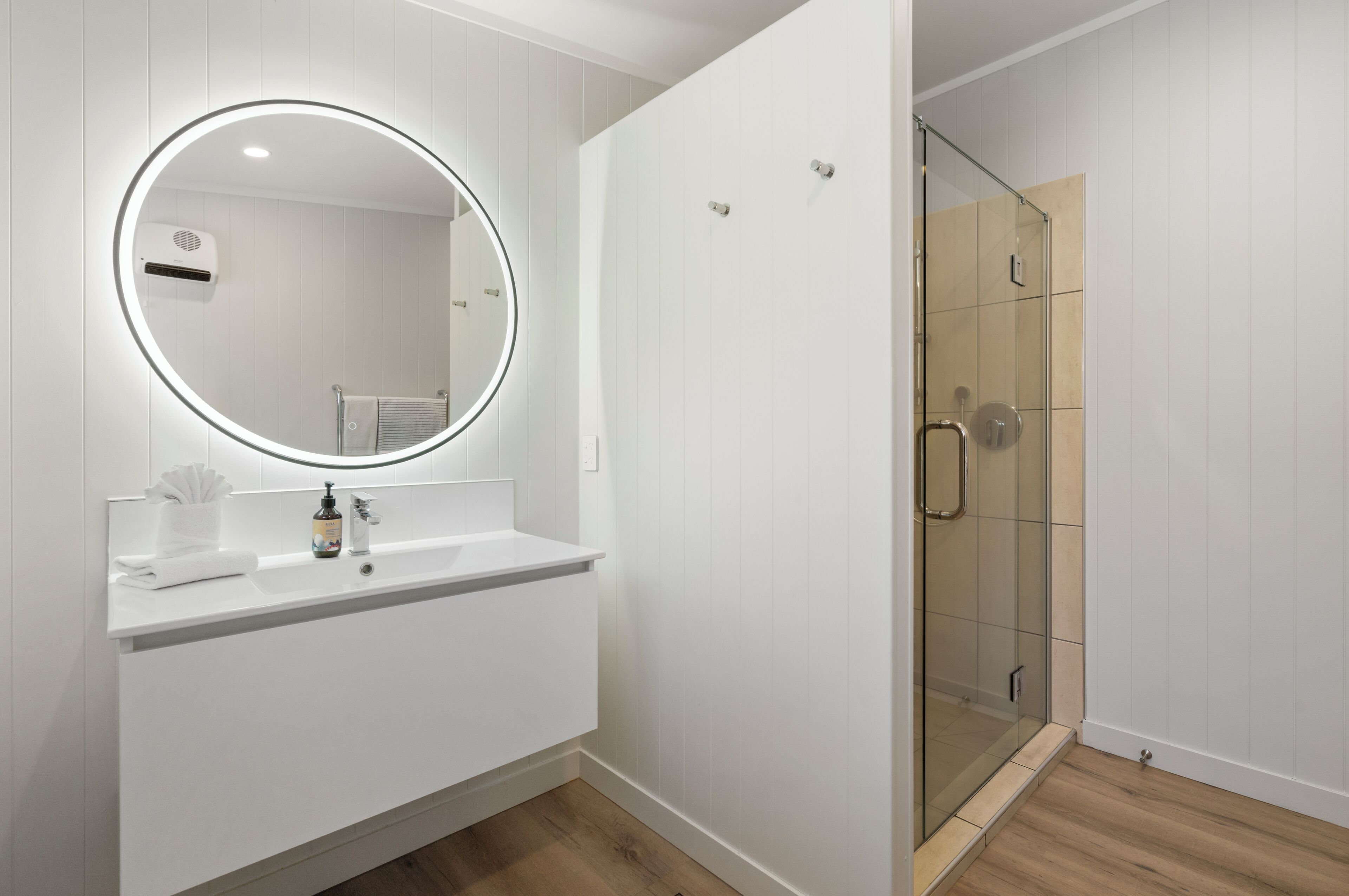 Un baño moderno con un espejo redondo, tocador blanco y cabina de ducha con mampara de vidrio.