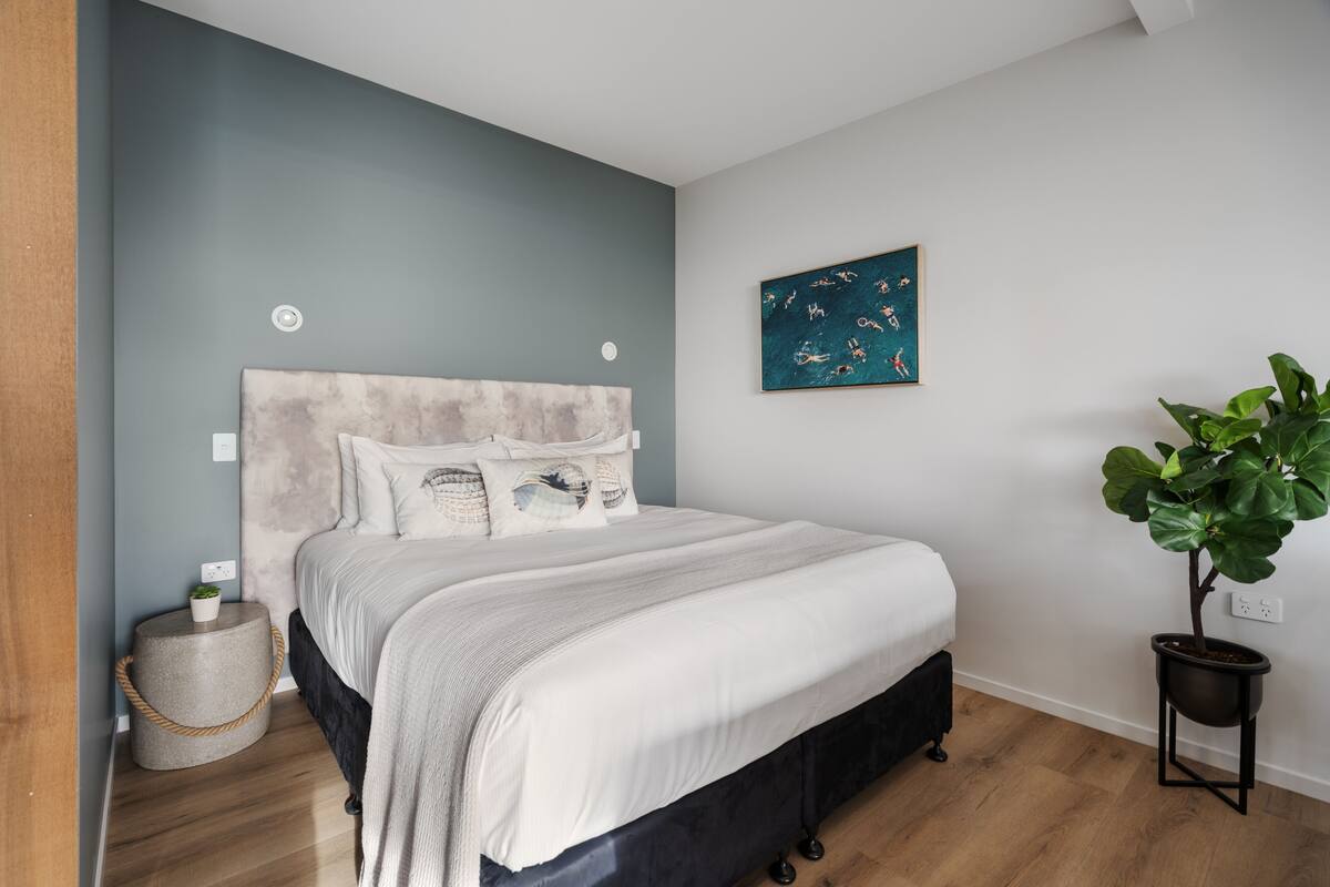 Ein Schlafzimmer mit Bett, Kopfteil, Wandkunst, Topfpflanze und Nachttisch.
