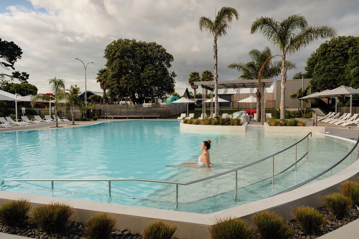 Une piscine avec une personne dans l’eau, entourée de chaises longues et de palmiers.