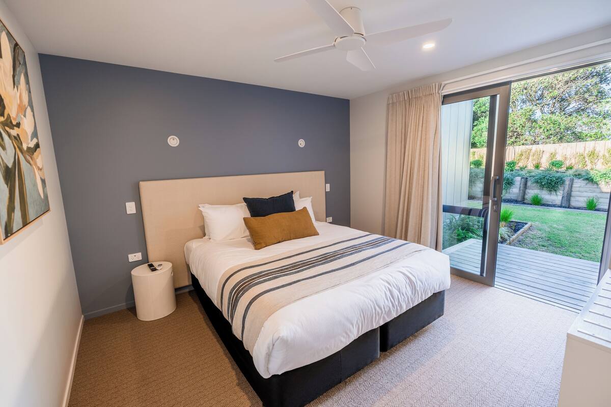 Ein Schlafzimmer mit einem Bett, einem Deckenventilator, einer kleinen Mülleimer und einer Glastür, die zu einem Balkon führt.