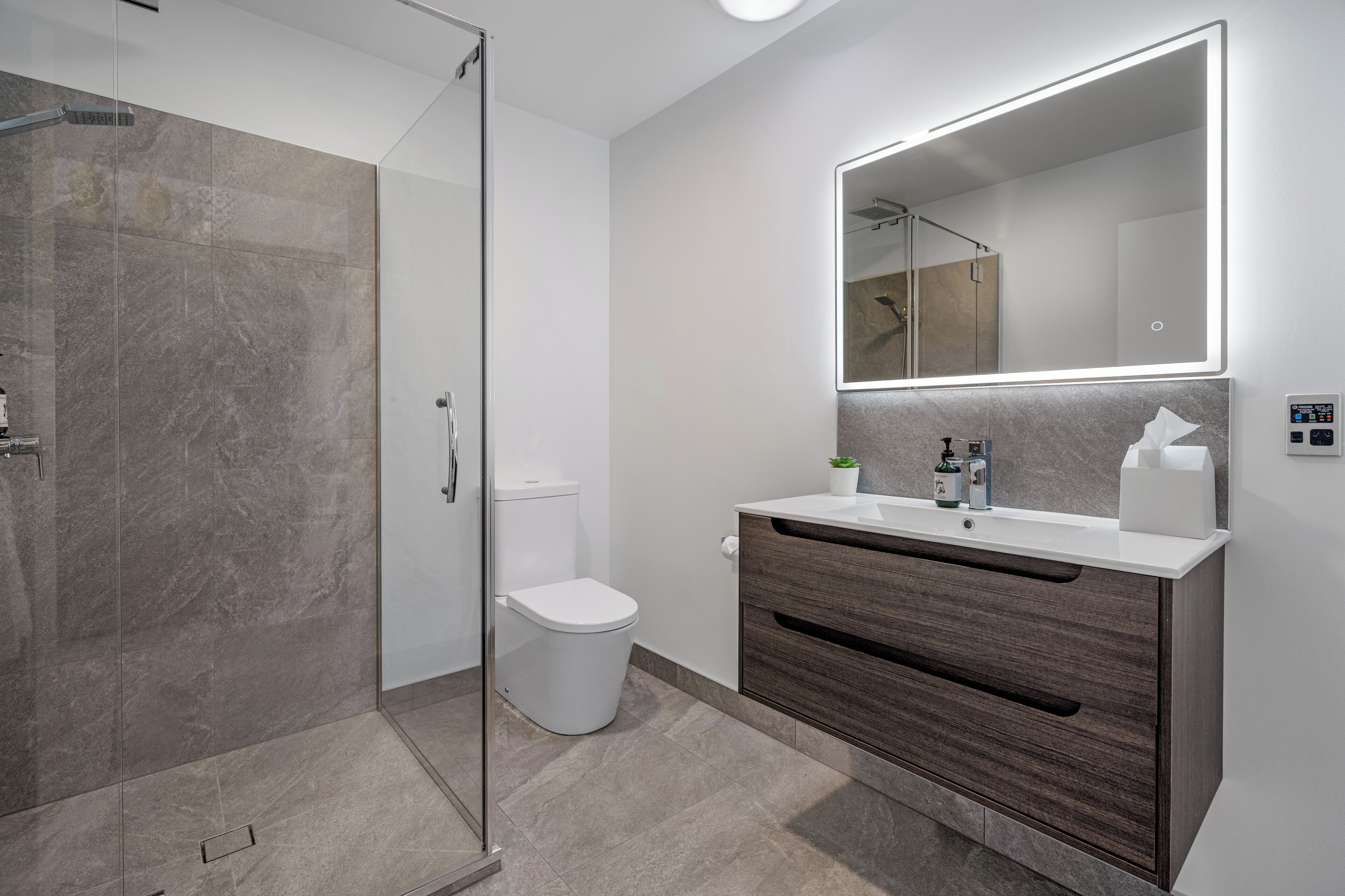 A modern bathroom with a glass shower enclosure, a white toilet, and a vanity with a mirror.