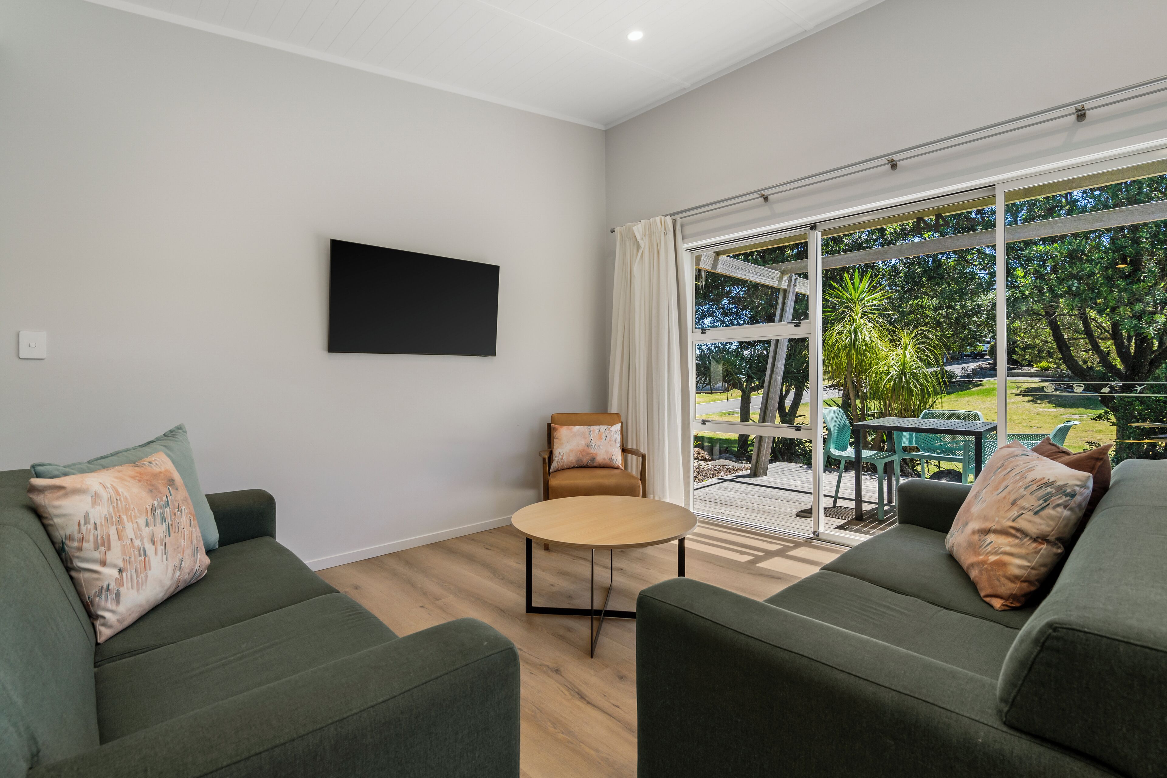 Una sala de estar moderna con un sofá verde, una mesa redonda de centro y vista a un patio exterior con una mesa y sillas.
