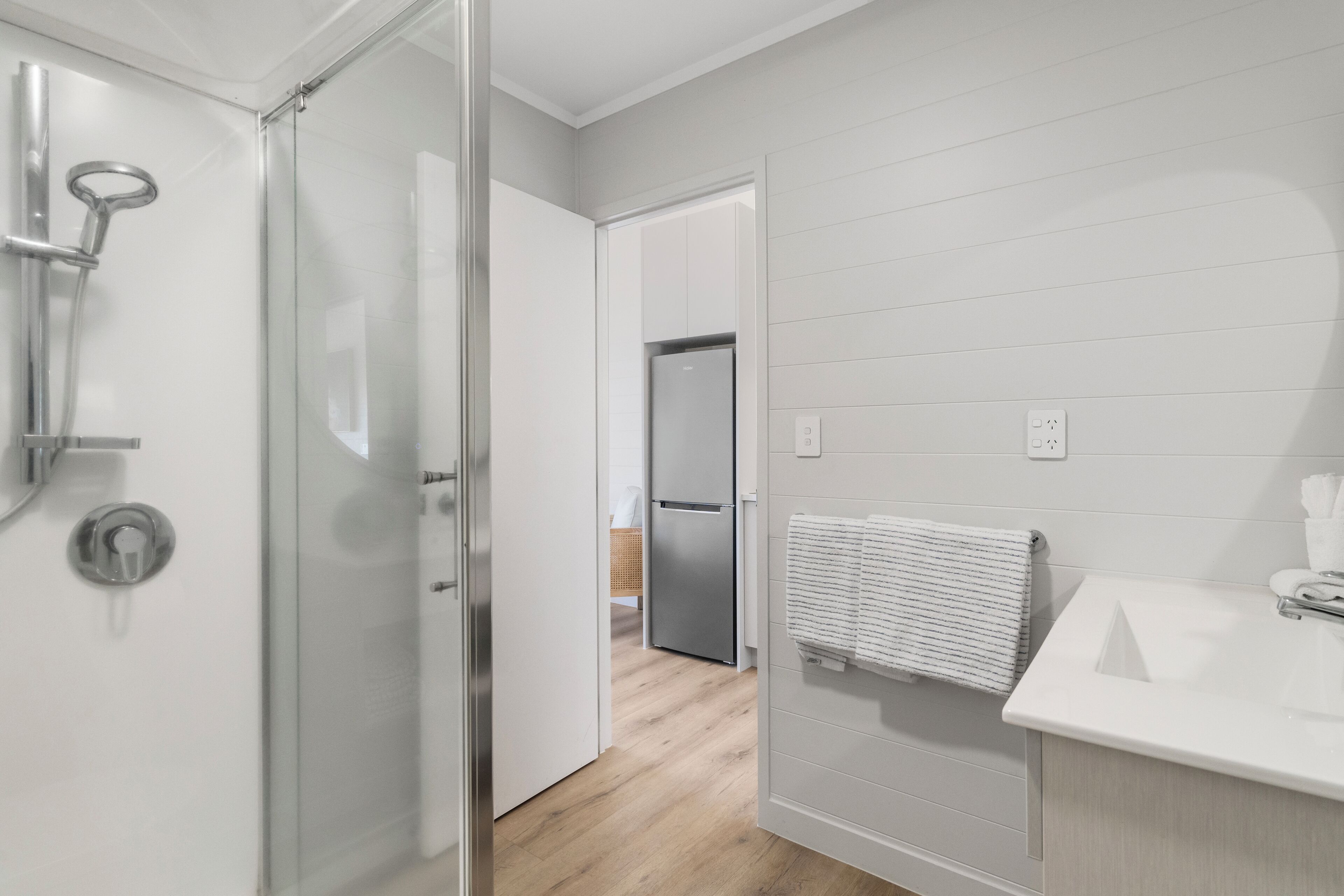A modern bathroom with a glass shower enclosure, a white sink, and a wooden floor.