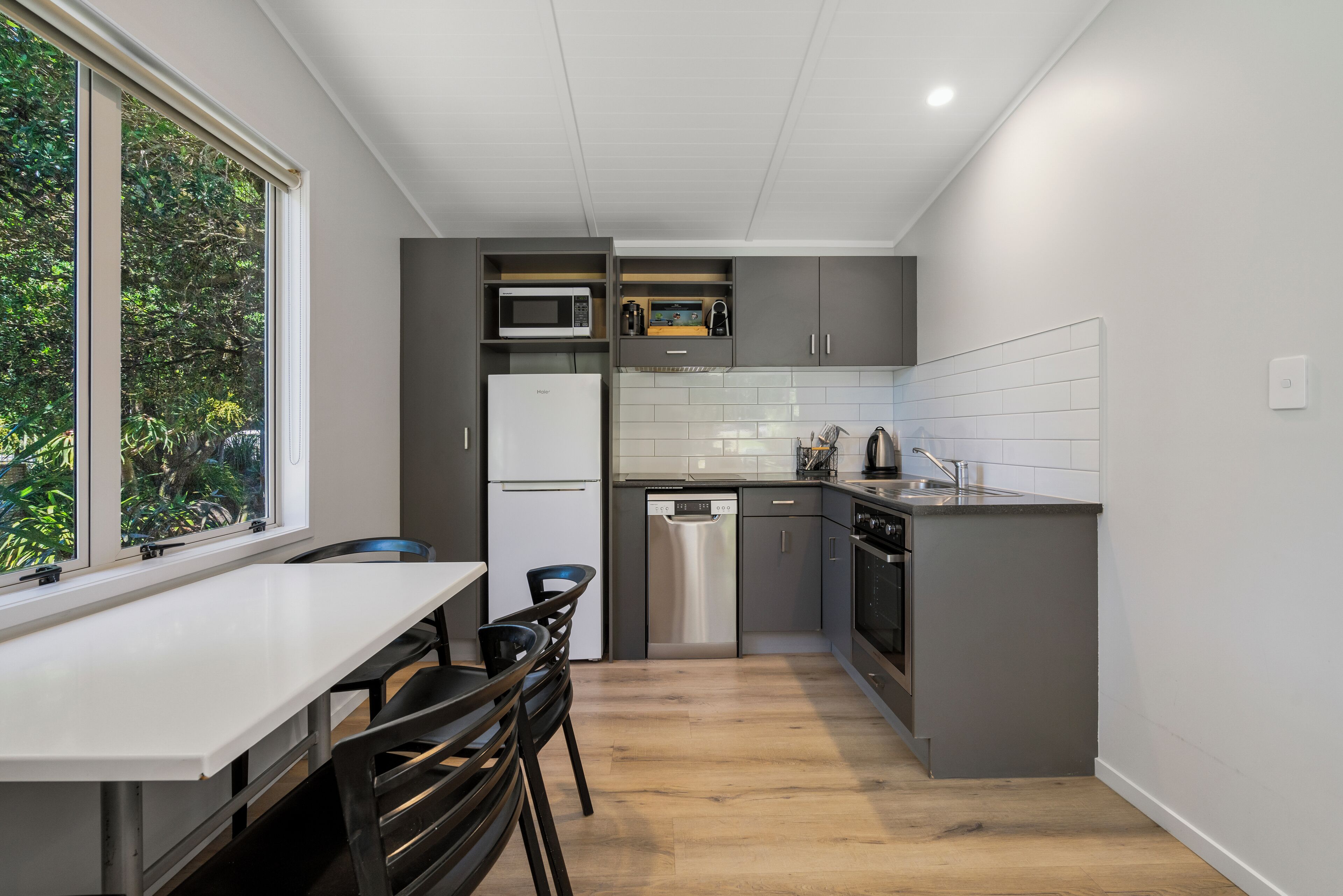 A compact kitchen with a white countertop, stainless steel appliances, and a view of greenery outside.