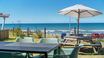 Un patio frente a la playa con mesas y sillas, una pérgola de madera y vistas al océano.