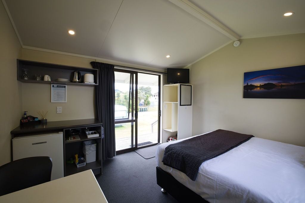 A hotel room with a bed, desk, and a view through the glass door.