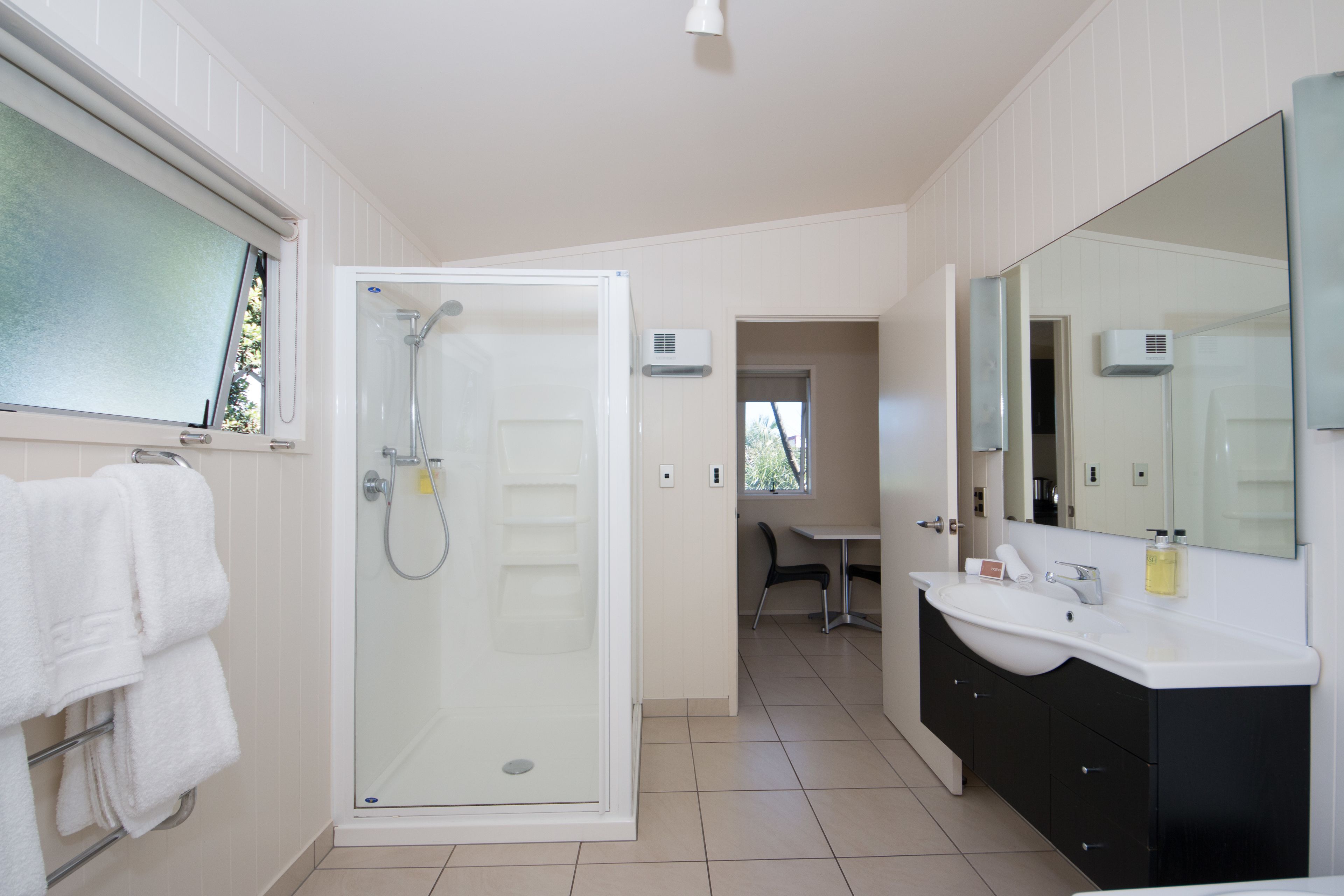 Un baño moderno con cabina de ducha de vidrio, un lavabo blanco y un espejo grande.