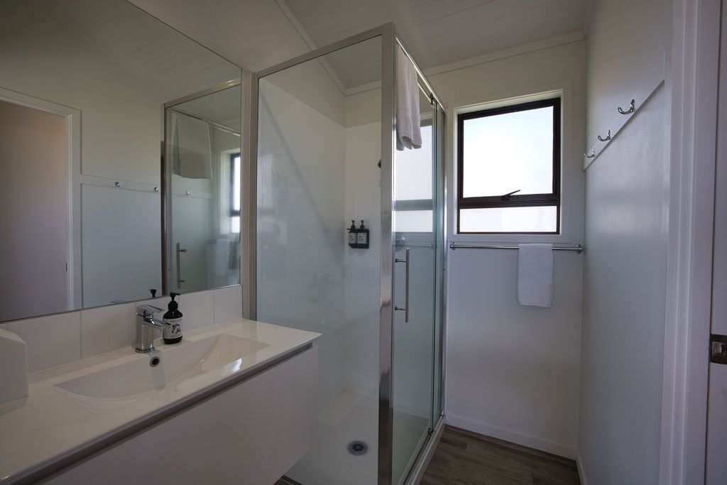Une salle de bain moderne avec une douche à parois de verre, un grand miroir et une fenêtre laissant entrer la lumière naturelle.