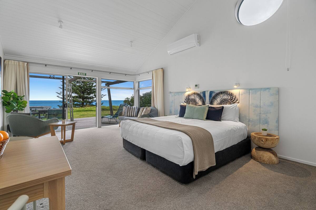 Ein modernes Schlafzimmer mit einem großen Bett, einem Esstisch und Blick auf den Ozean.